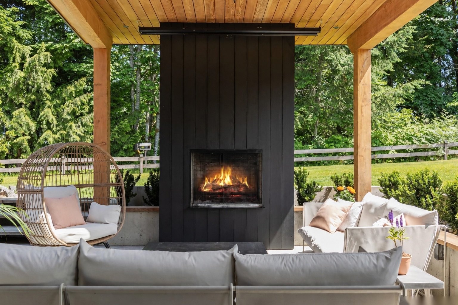 Outdoor lounge with black-clad fireplace under a timber ceiling